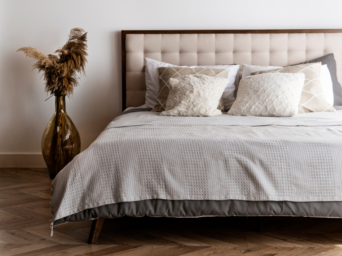 Cama com cabeceira estofada, roupa de cama cinza e travesseiros decorativos em um quarto moderno.