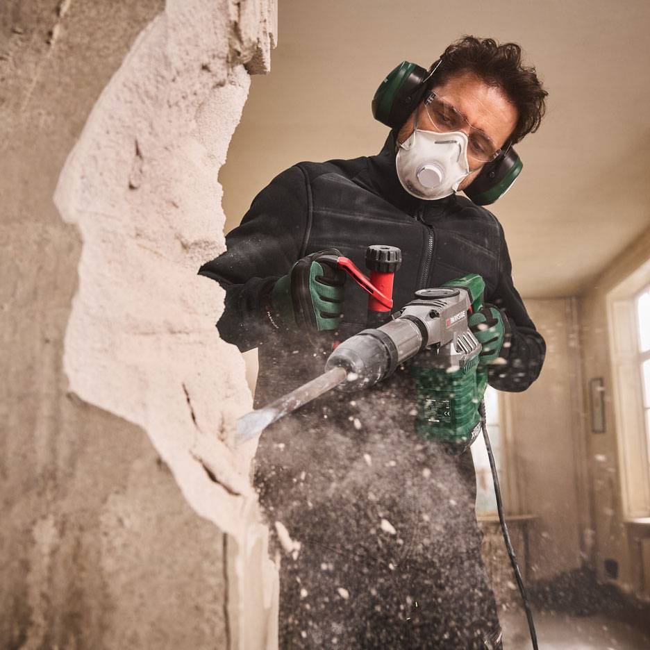 Homem com martelo demolitor e equipamento de proteção a demolir uma parede.