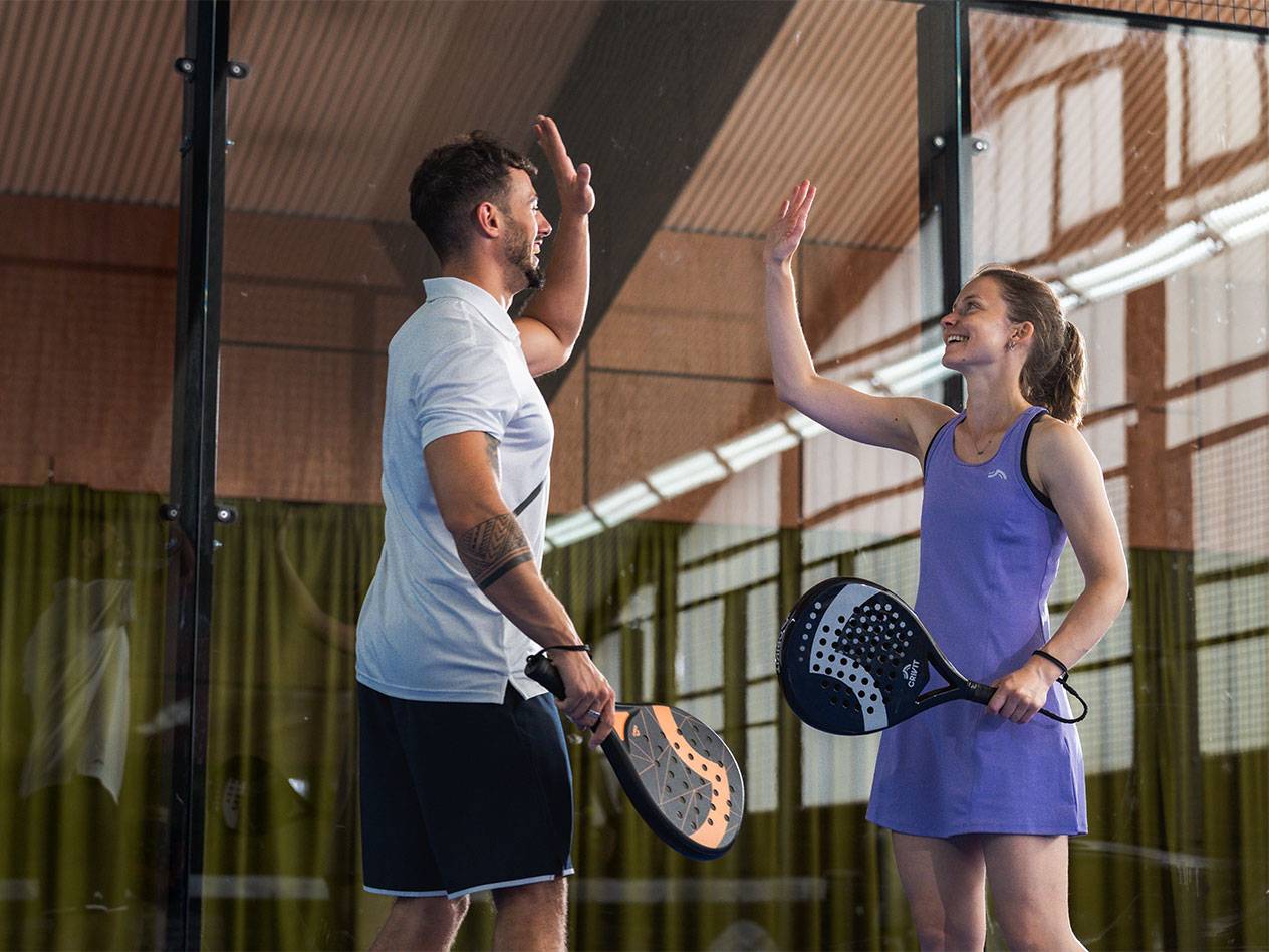 Dois jogadores de padel, um homem e uma mulher, a fazer um high-five no campo.