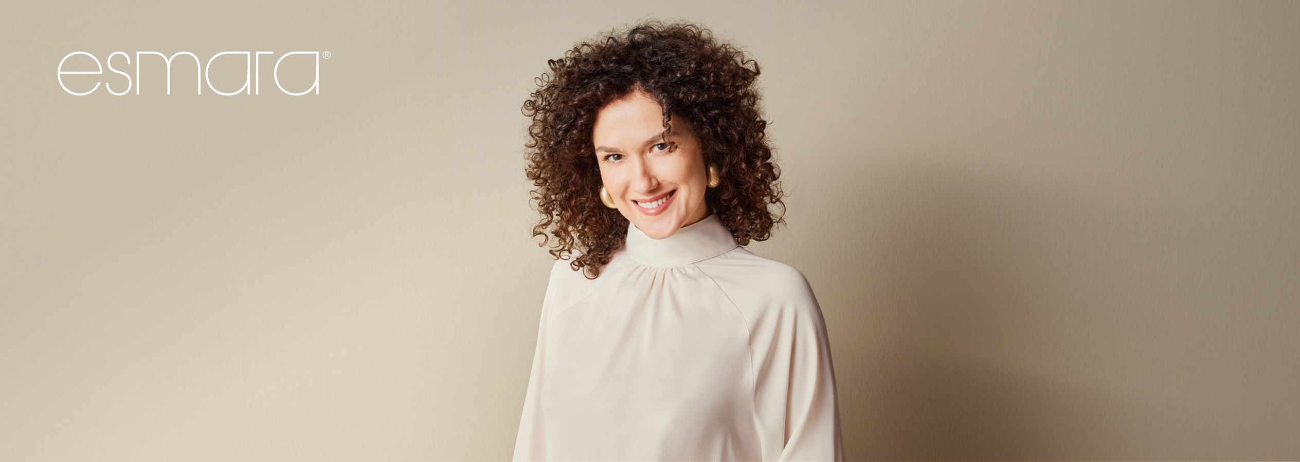 Mulher sorridente com cabelo encaracolado e blusa bege, com o logótipo Esmara.