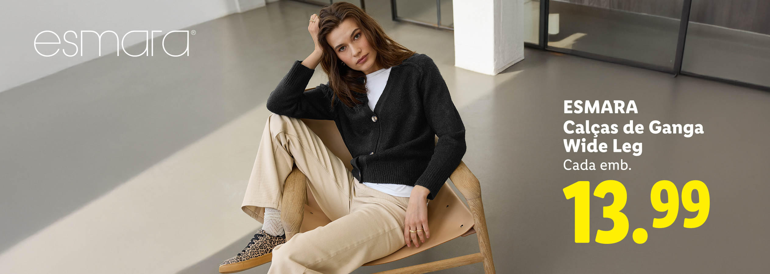 Mulher sentada a usar um cardigan preto e calças de ganga wide leg bege, preço 13.99.