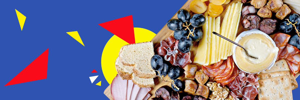 Queijos, frios, pão e uvas em uma tábua.