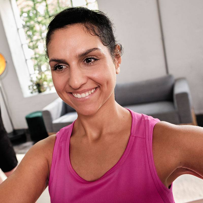 Mulher sorridente com camiseta rosa se exercitando em casa.