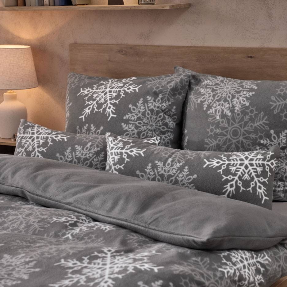 Roupa de cama cinzenta com flocos de neve brancos, com almofadas e um cobertor fofo.