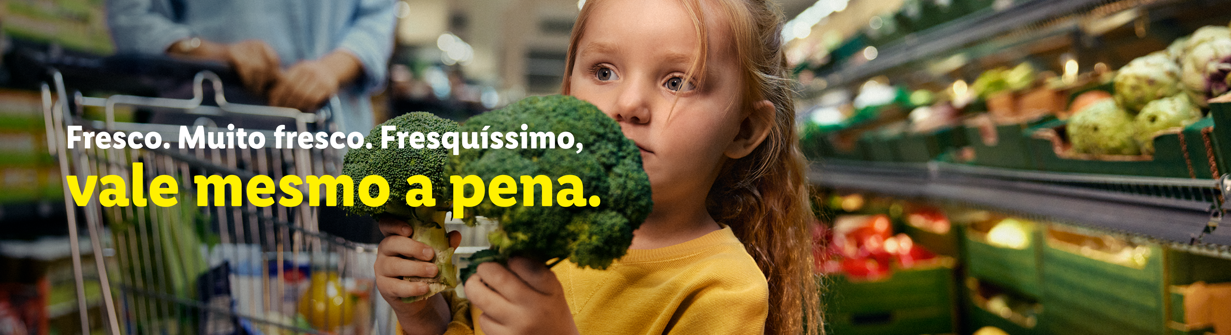 Uma criança segura brócolos num supermercado, com o texto 'Fresco. Muito fresco. Fresquíssimo, vale mesmo a pena.'