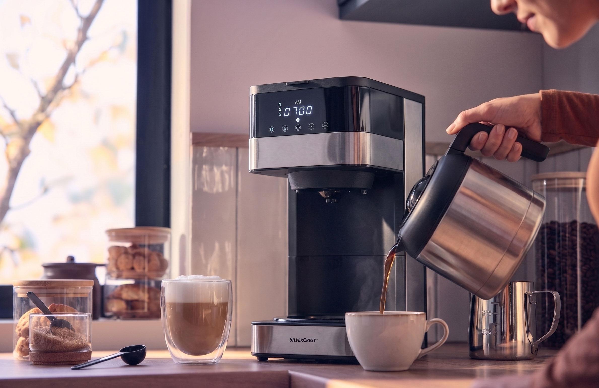 Máquina de café a servir café numa chávena, com um latte e biscoitos no balcão.
