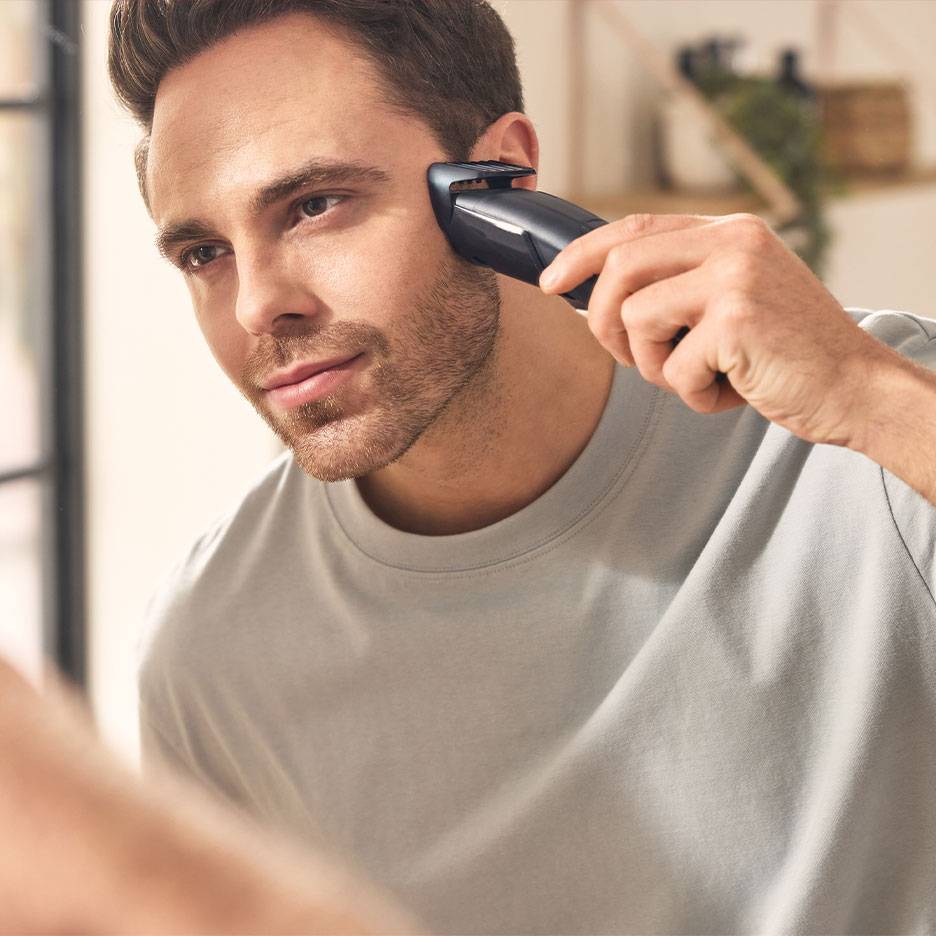 Homem a aparar a barba com um aparador de barba em frente ao espelho.