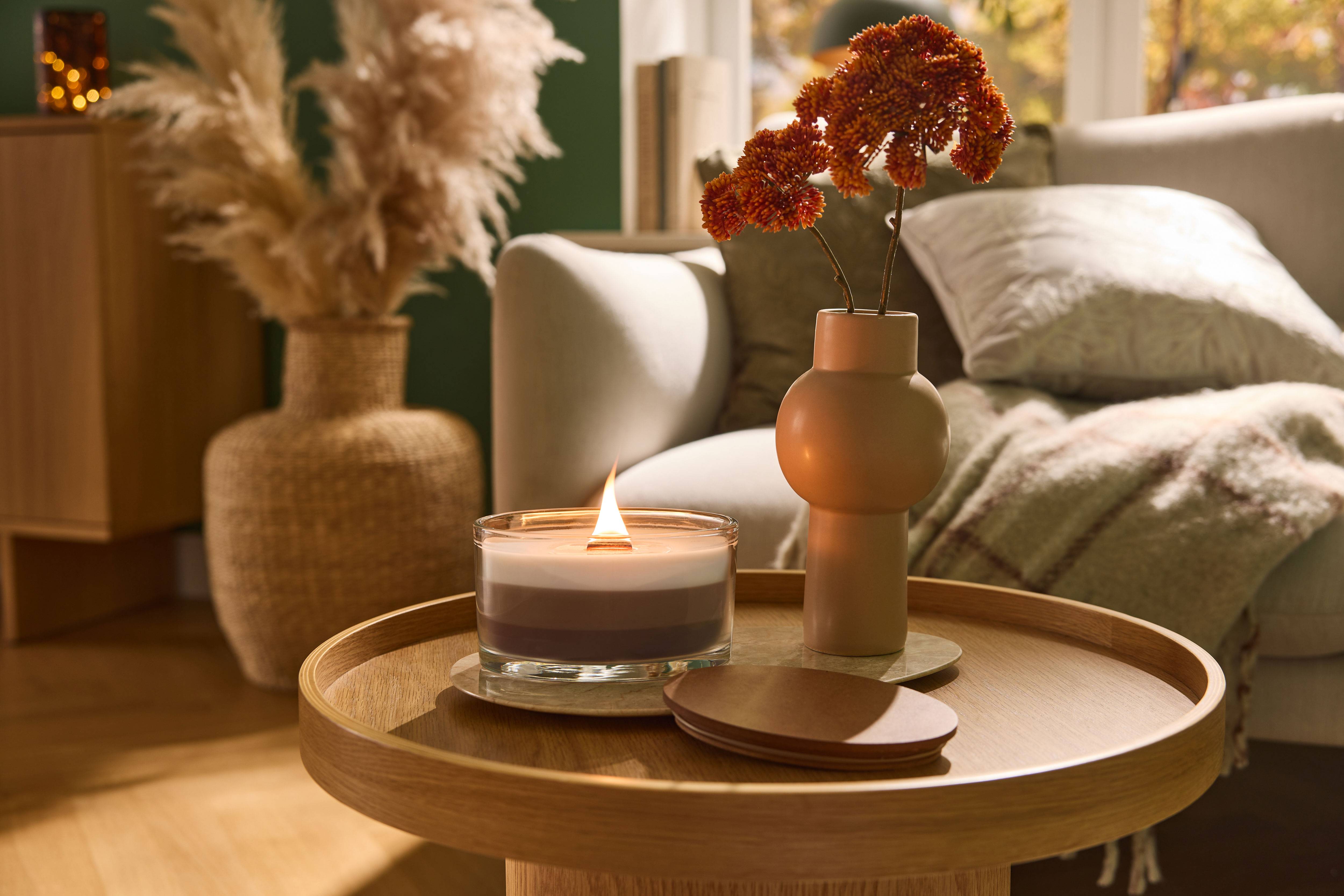 Vela acesa e vaso com flores numa mesa de centro de madeira na sala de estar.