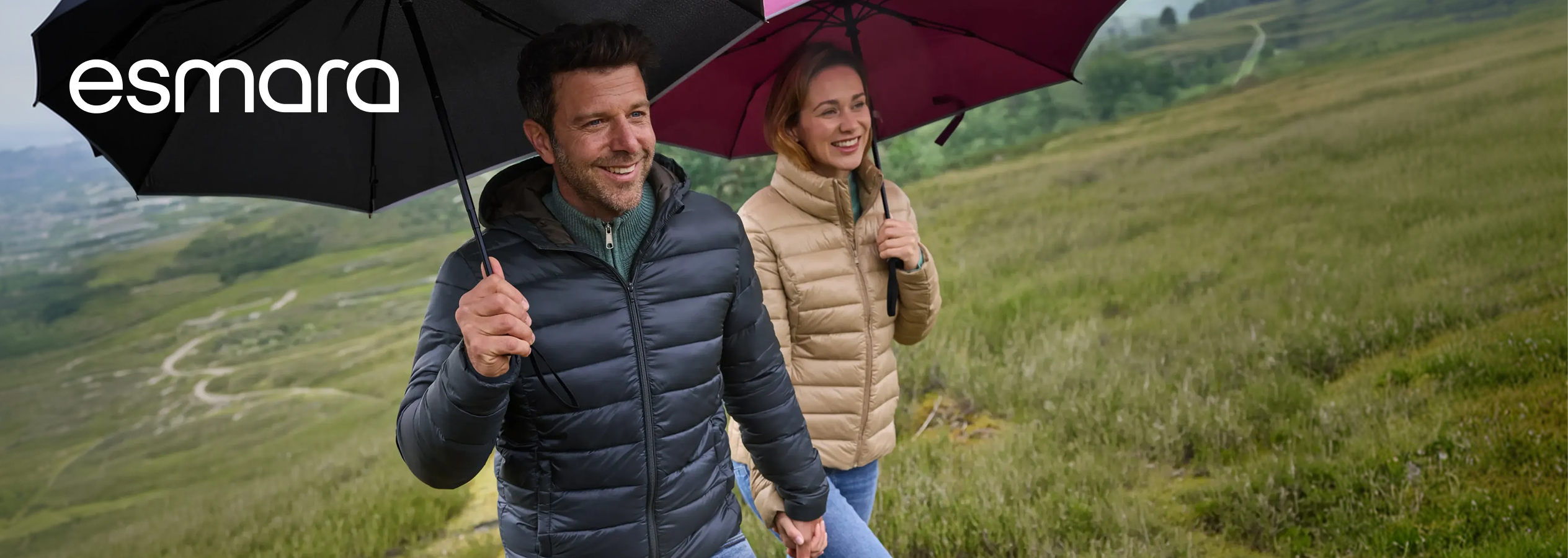 Esmara: Casal a caminhar sob a chuva com guarda-chuvas e casacos acolchoados.