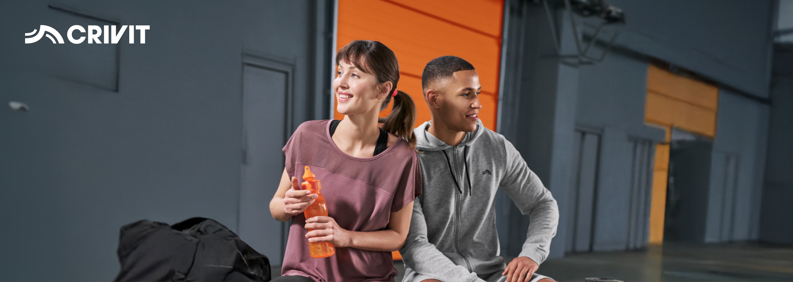 Dois atletas, um homem e uma mulher, sentados e a sorrir, com uma garrafa de água.