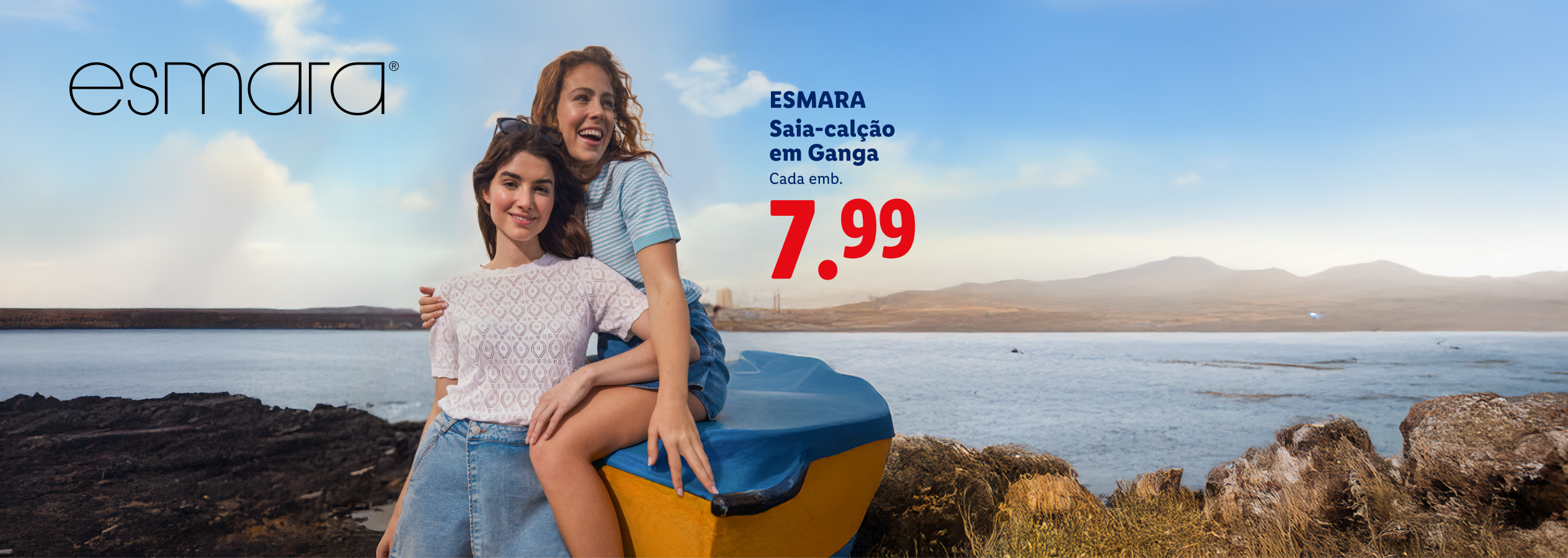 Duas mulheres sorridentes junto ao mar, uma delas sentada num barco, com saia-calção em ganga a 7,99€.