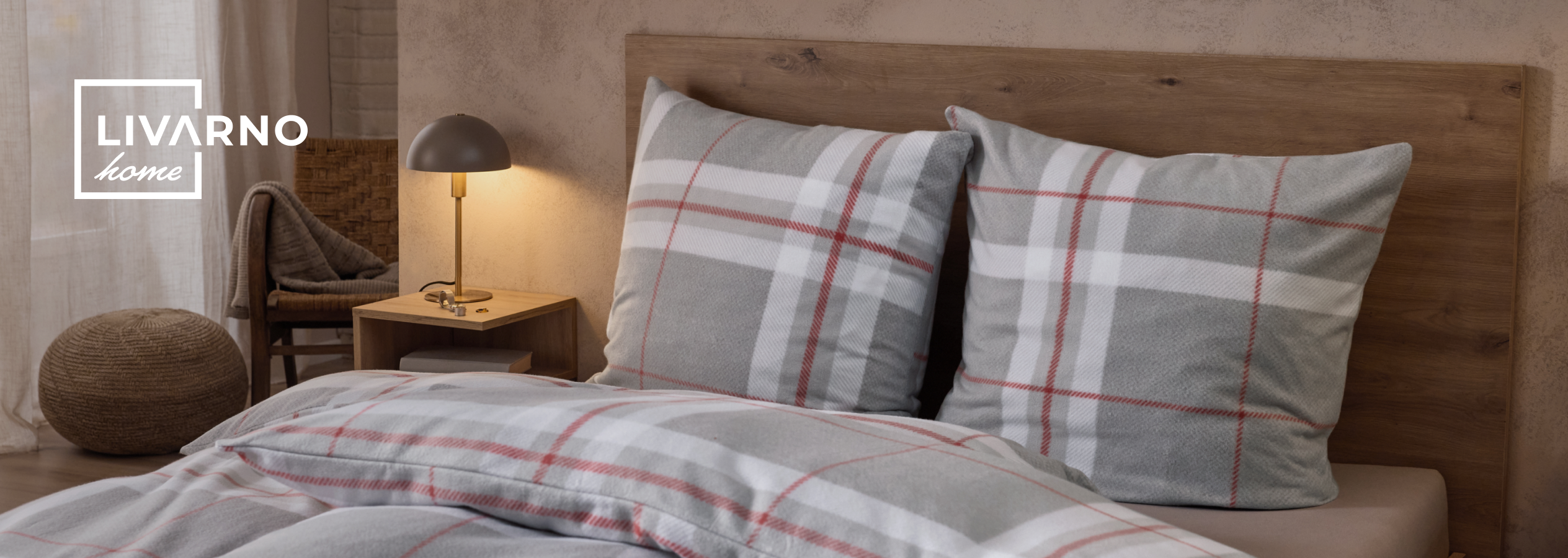 Cama com roupa de cama xadrez cinzenta e vermelha, mesa de cabeceira com candeeiro e pufe.