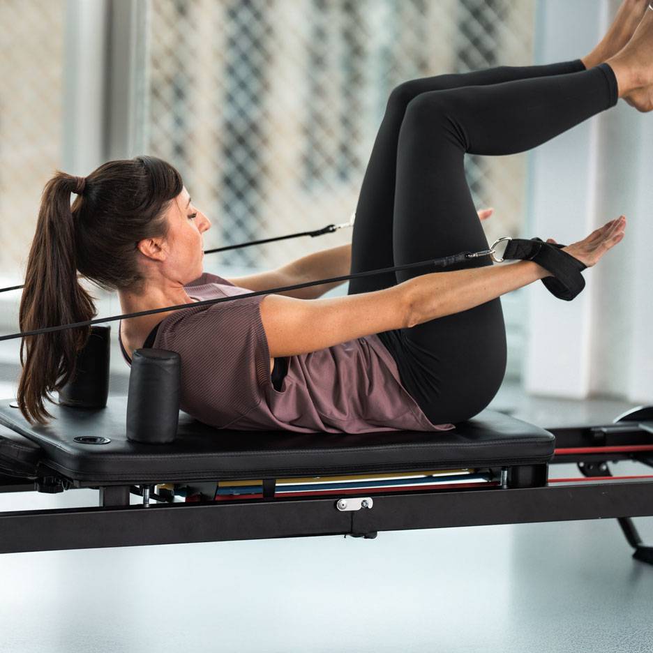 Mulher a praticar Pilates num reformer, vestindo roupa desportiva preta.