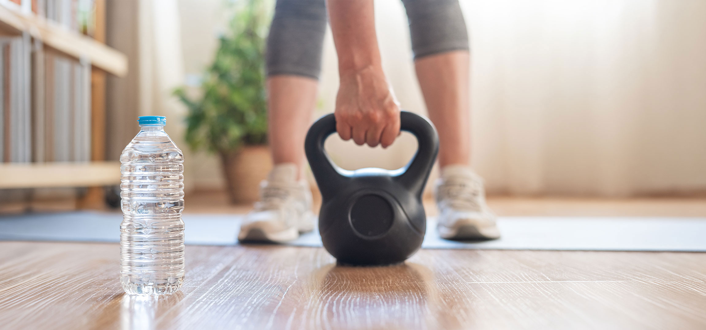 aiLabeling.aiLabelForImageAltText: Mulher prepara-se para treinar com um kettlebell e uma garrafa de água num tapete de ioga.
