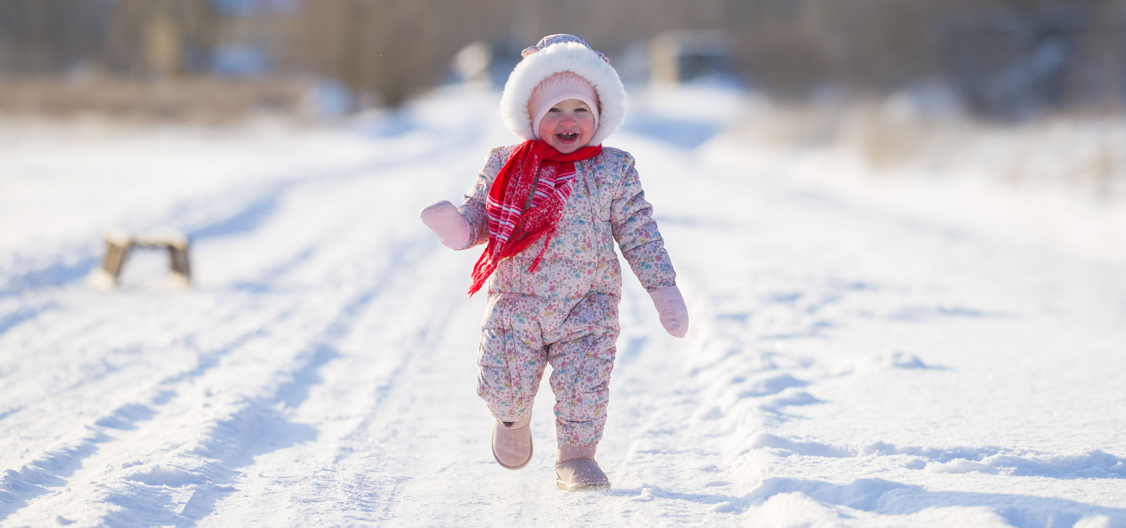 Menina alegre com fato de neve e cachecol a correr num caminho nevado.