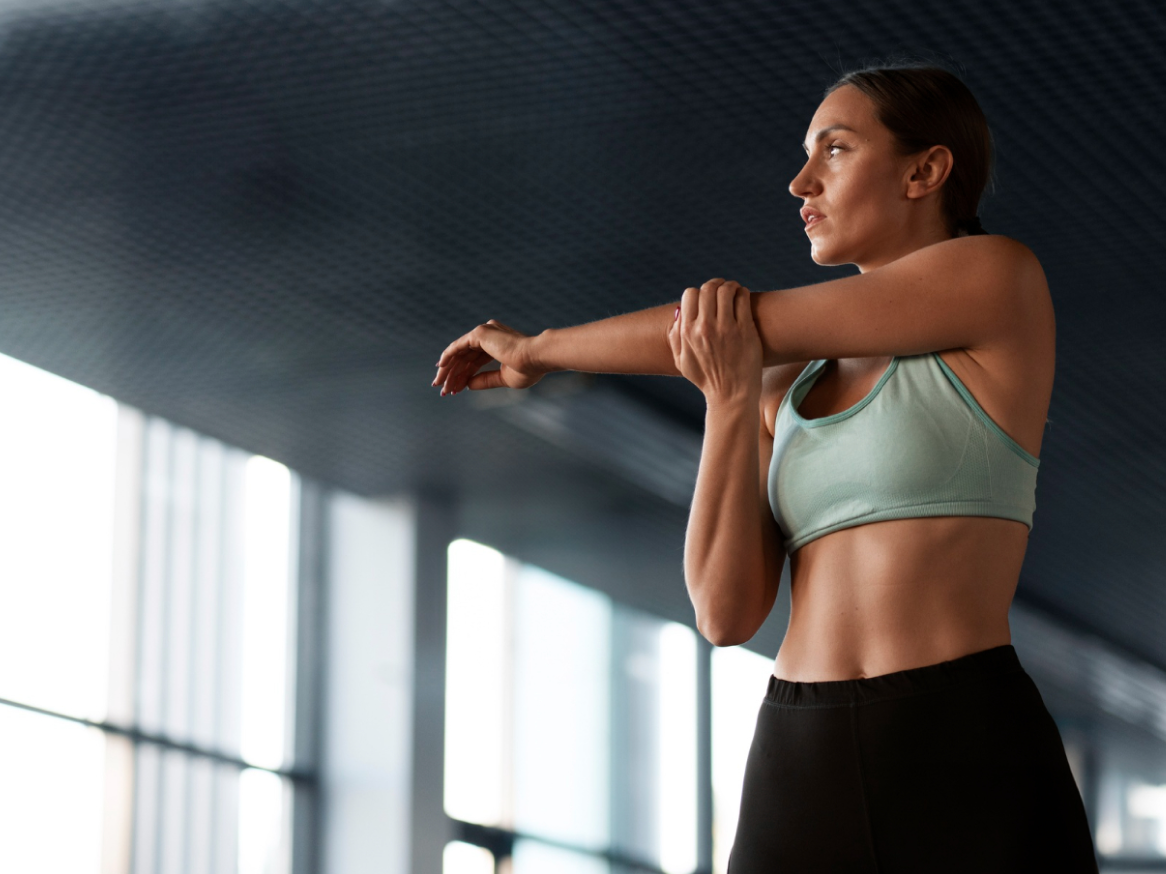 Mulher a alongar o braço, vestindo um top desportivo e leggings.