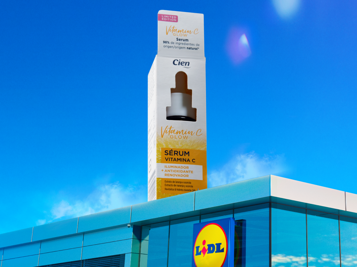 Um sérum de vitamina C em embalagem gigante, com um edifício de loja ao fundo.
