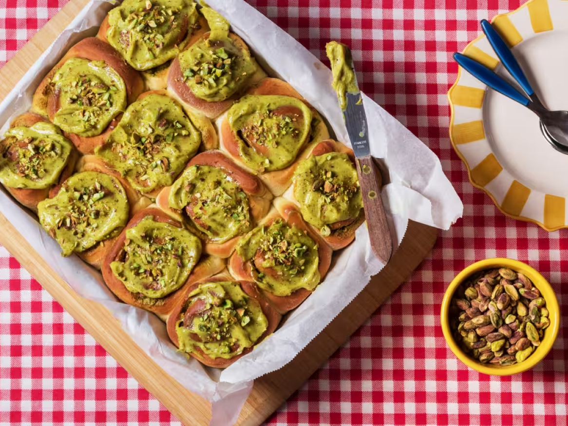 Pãezinhos de pistácio com cobertura verde e pistácios picados numa assadeira.