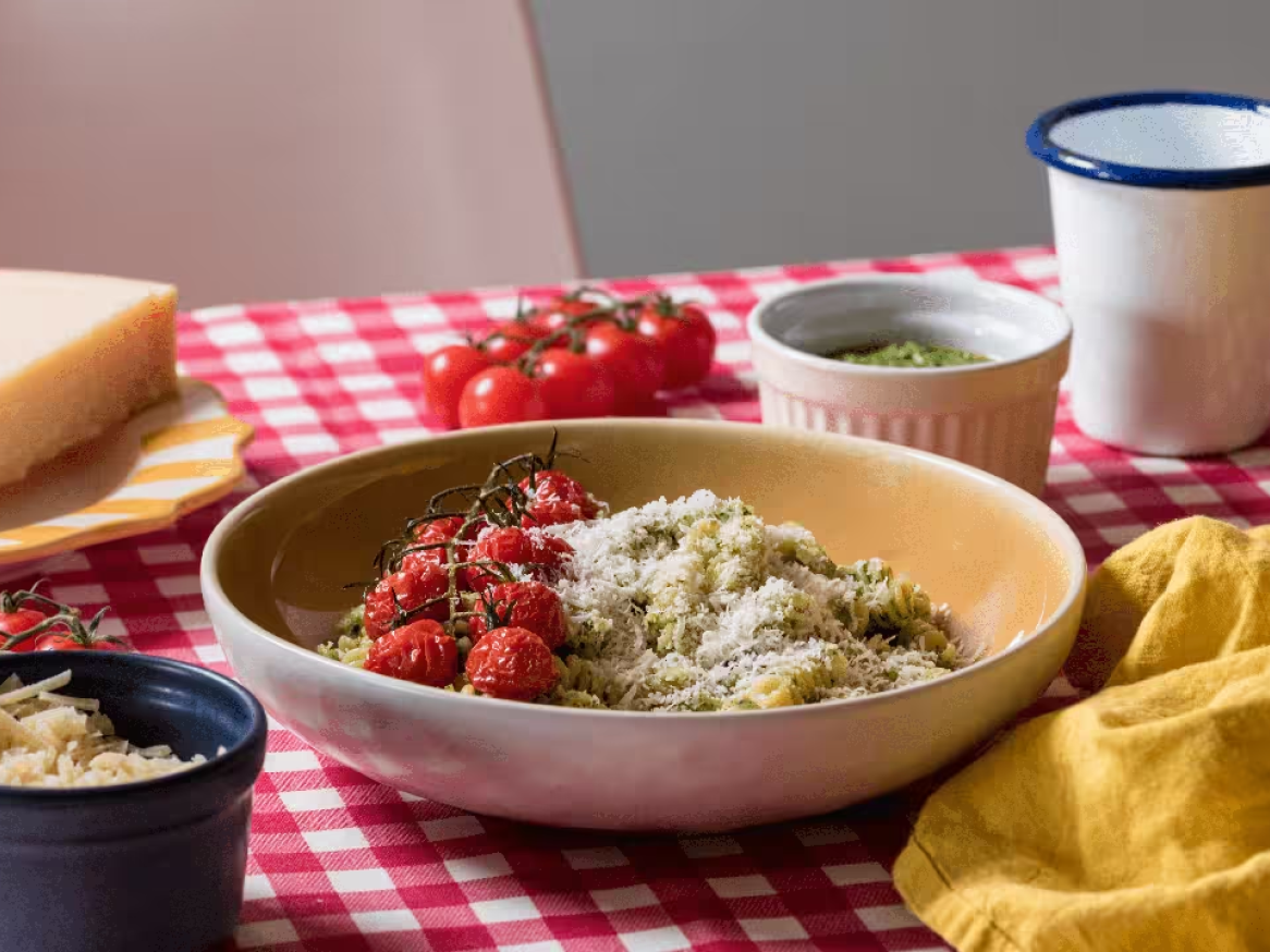 Massa com pesto, tomate assado e queijo ralado numa mesa com toalha xadrez.