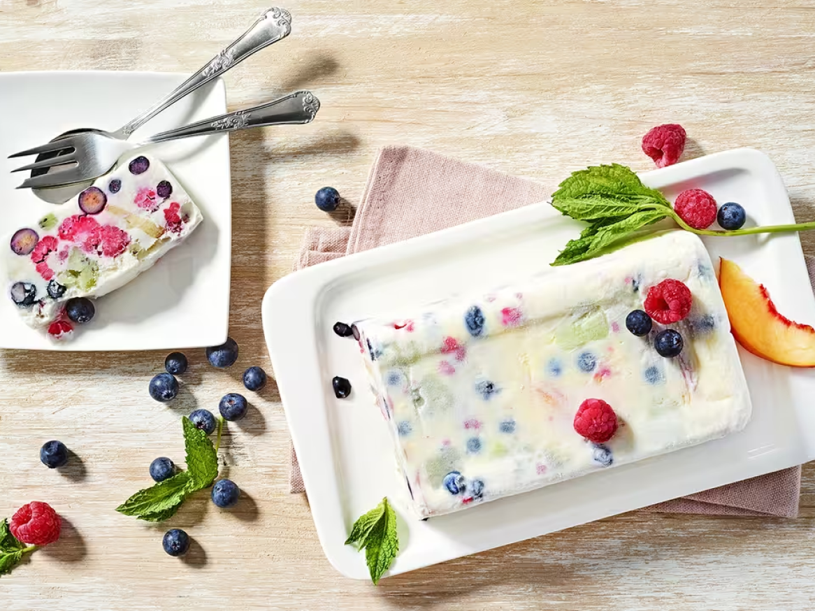 Semifreddo de frutos silvestres e pêssego em pratos brancos com talheres.