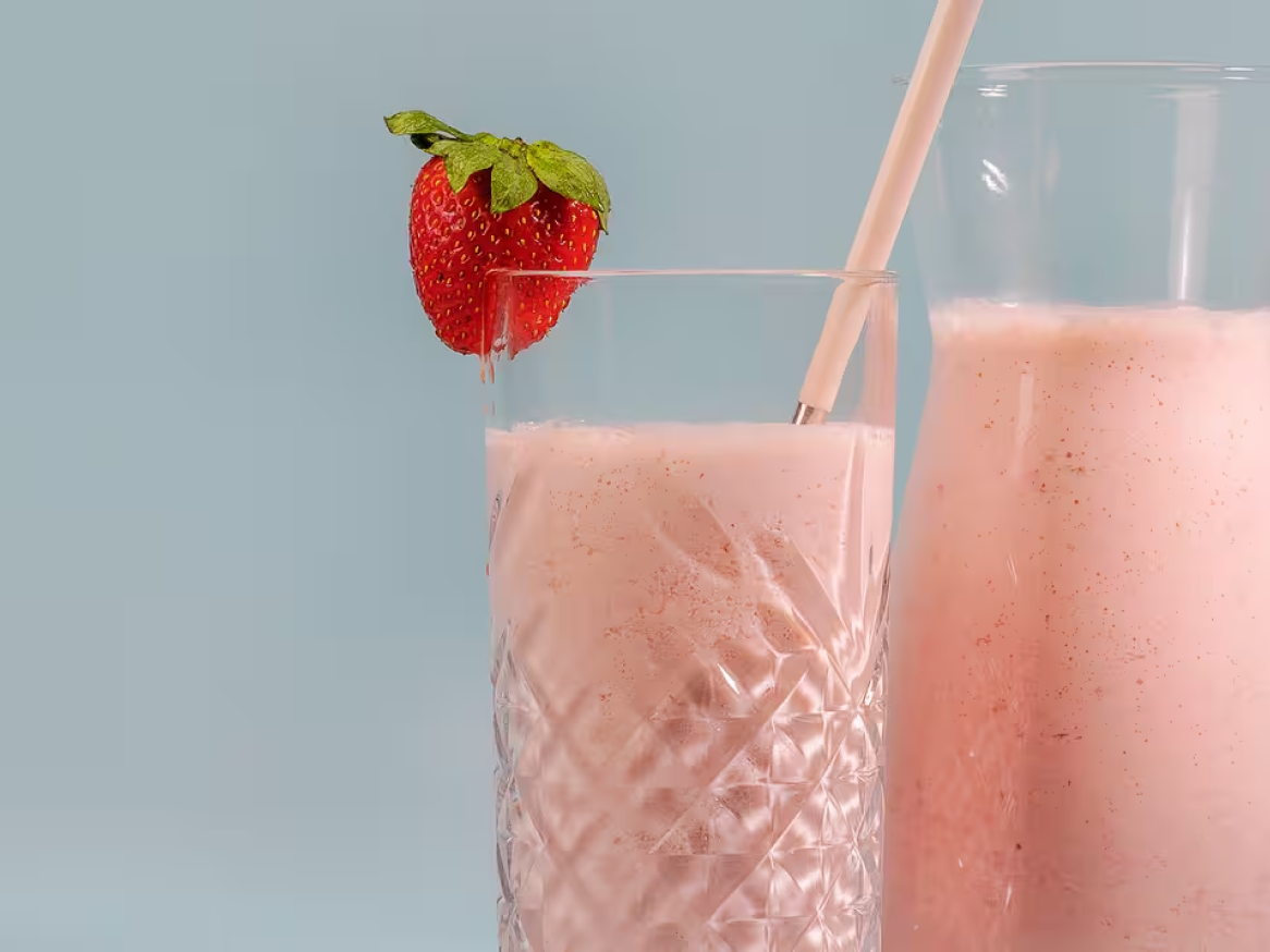 Batido de morango em copo e jarro com morango fresco e palhinha.