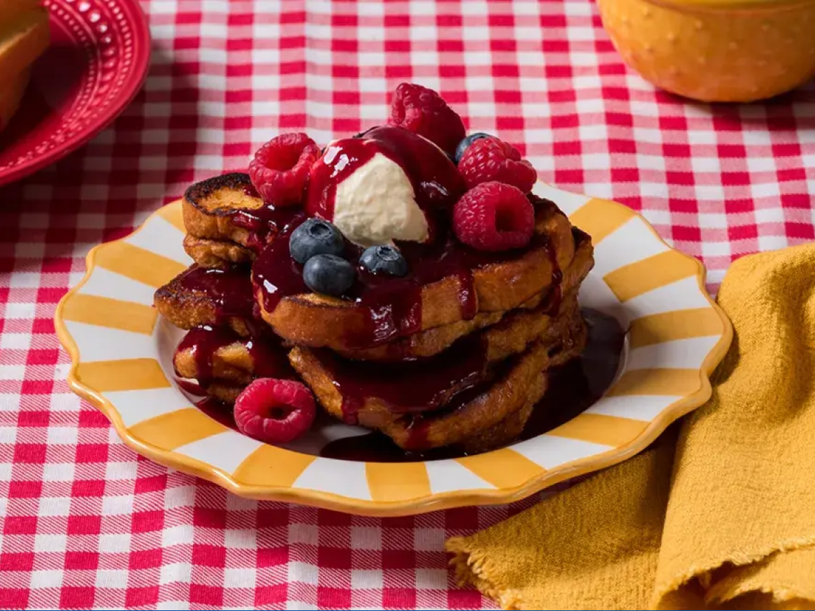 Torradas francesas com frutos silvestres, xarope e chantilly numa toalha de mesa xadrez.