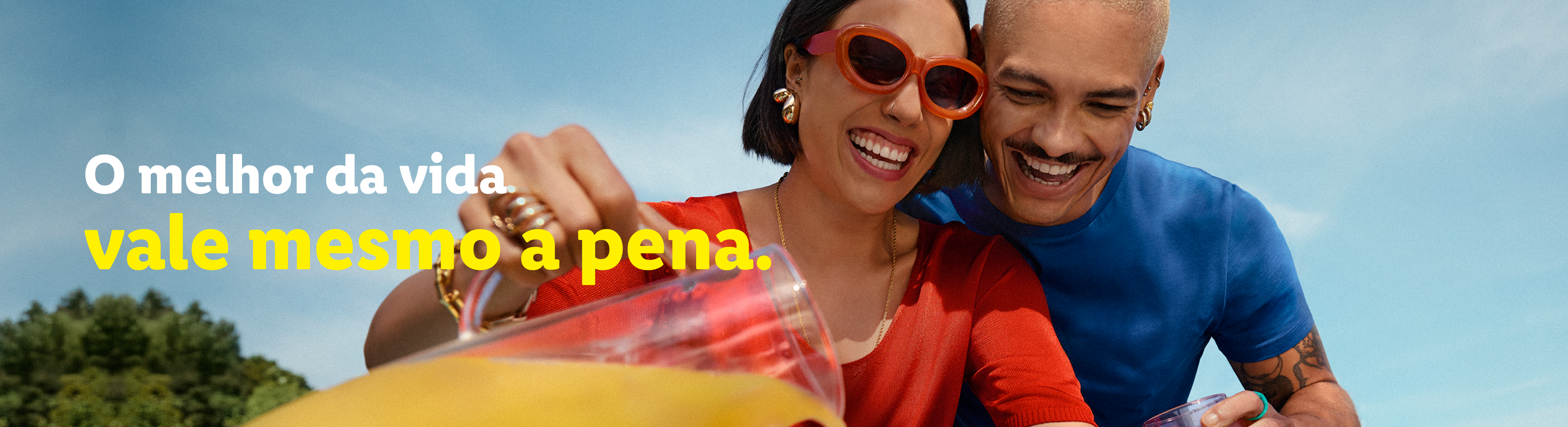 Um casal sorridente, com a mulher servindo uma bebida de um jarro para o homem.