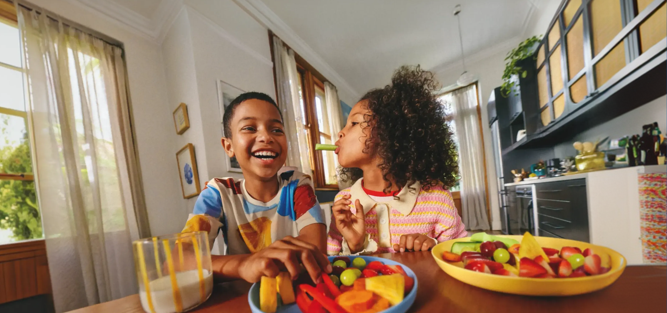 Duas crianças felizes a desfrutar de uma taça de fruta fresca e colorida.