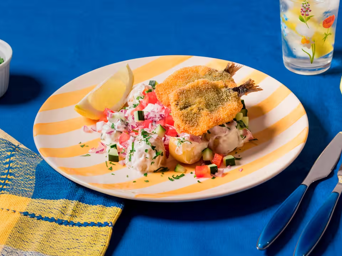 Peixe frito com molho de iogurte, pepino, tomate e cebola roxa, servido com limão.