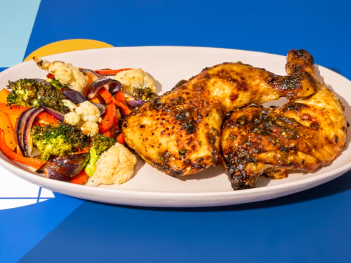 Frango assado com vegetais assados, incluindo brócolos, couve-flor e pimentos.