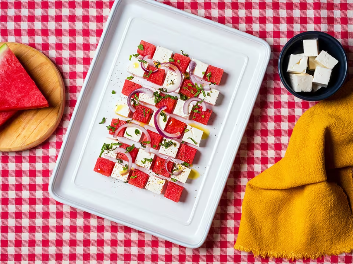 Salada de melancia e queijo feta com cebola roxa e hortelã, sobre toalha xadrez.