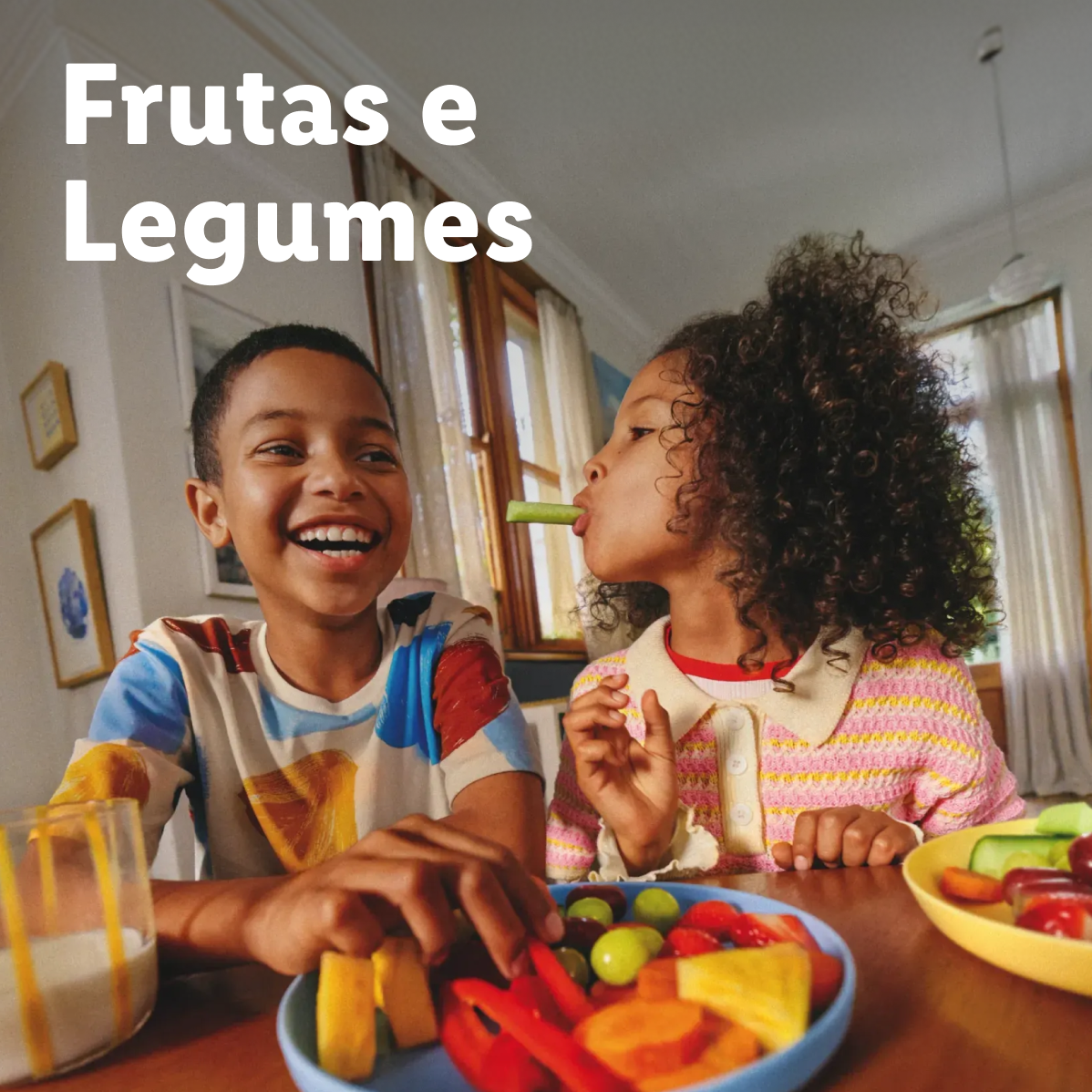 Duas crianças felizes a comer frutas e legumes frescos. Texto: Frutas e Legumes.