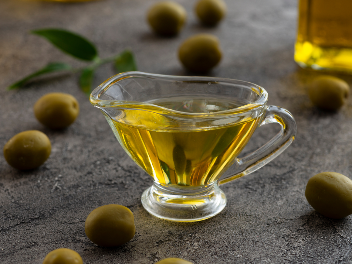 Azeite em molheira de vidro com azeitonas verdes e folha de oliveira.