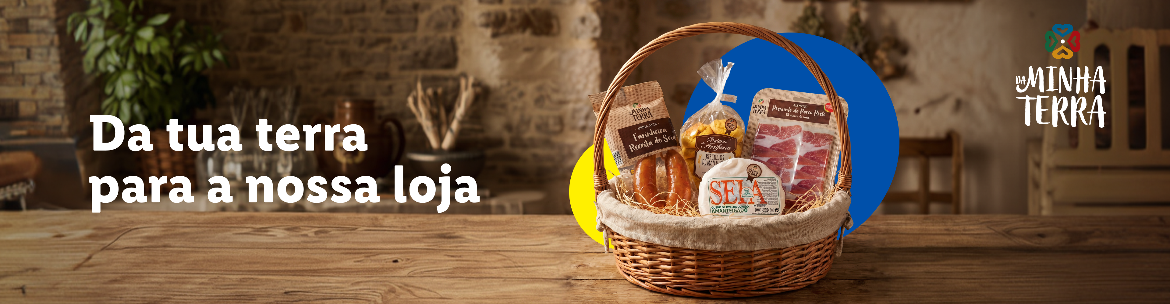 Cesto de produtos regionais com farinha, biscoitos, presunto, queijo e enchido, com o tema 'Da tua terra para a nossa loja'.