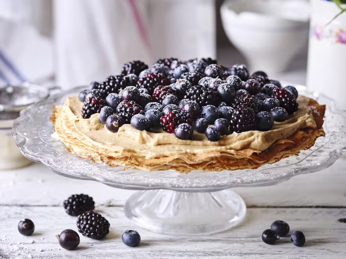 Bolo de crepe com creme e frutos silvestres, polvilhado com açúcar em pó.