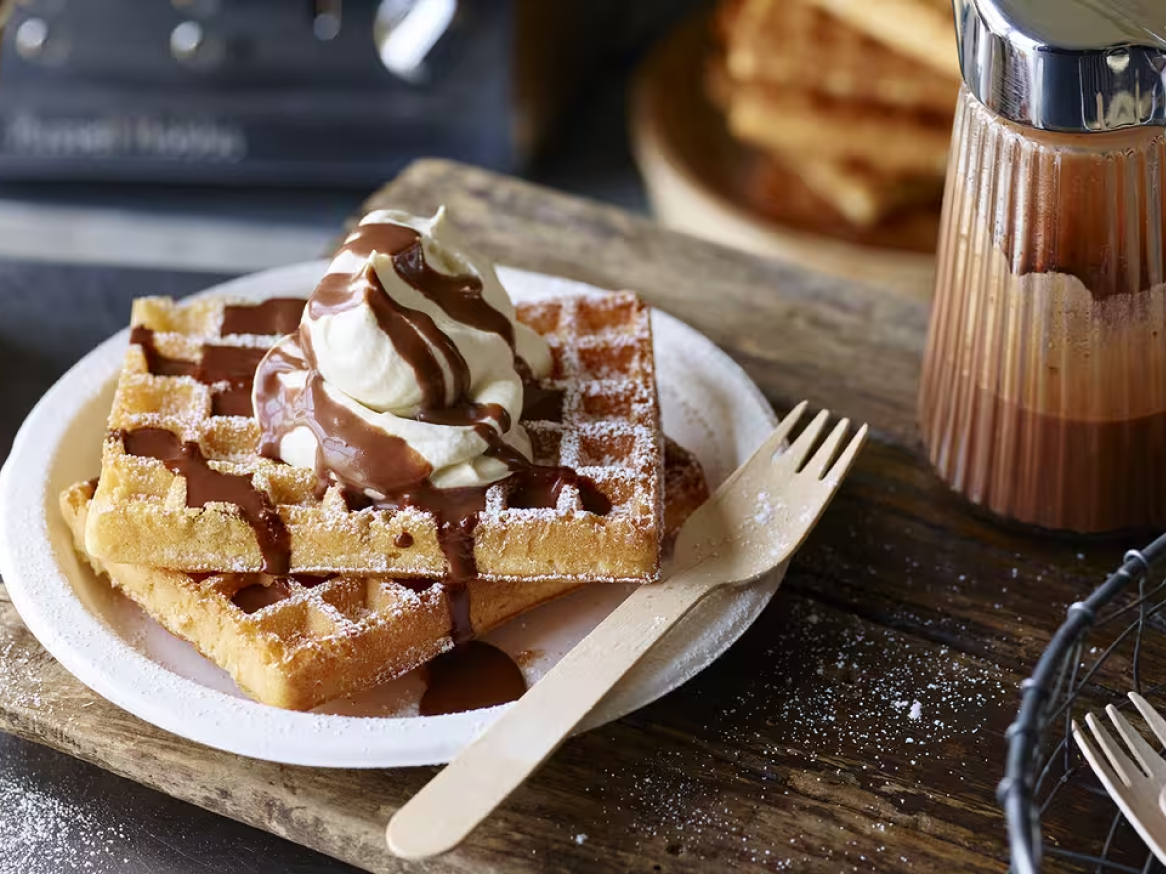 Waffles com chantilly, calda de chocolate e açúcar em pó, servidos num prato branco.