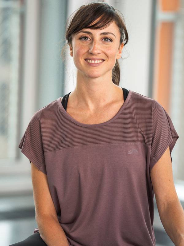 Mulher sorridente a usar um top desportivo roxo de manga curta.