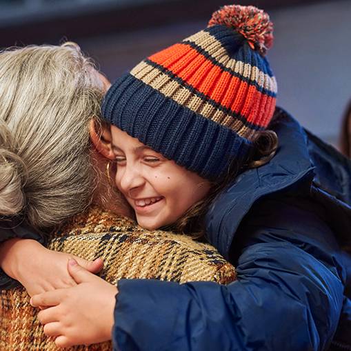 Criança feliz com gorro de inverno a abraçar uma pessoa mais velha.