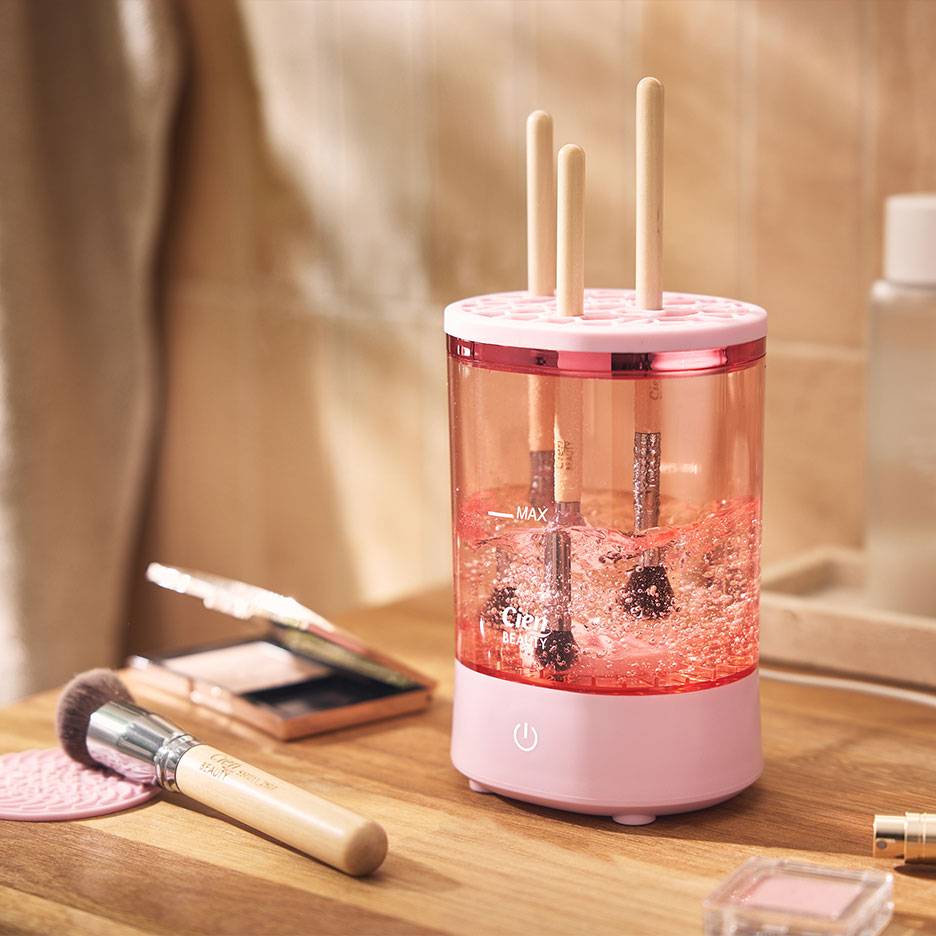Aparelho rosa para limpar pincéis de maquilhagem com pincéis em água espumosa.