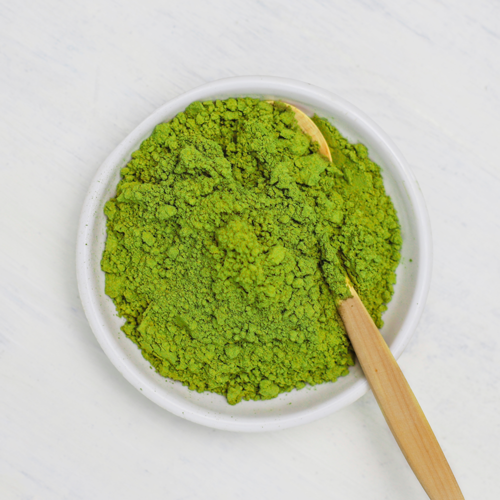 Pó verde vibrante numa tigela branca com uma colher de madeira.