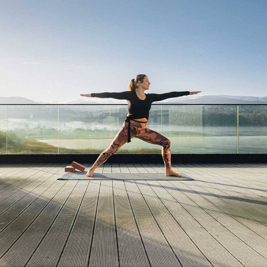 Mulher de leggings e top desportivos a fazer ioga num terraço com vista.