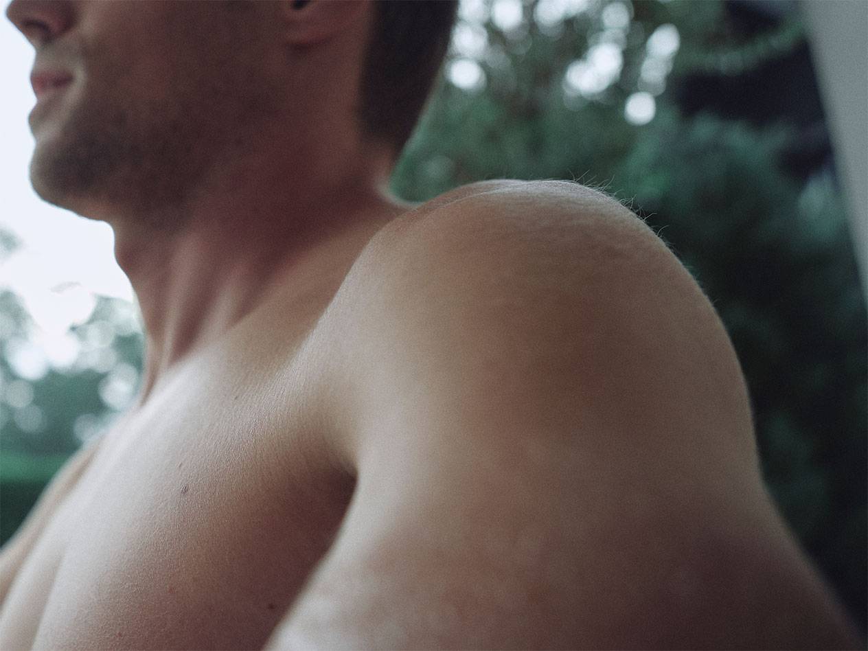 Close-up do ombro e pescoço de um homem, com um fundo verde desfocado.