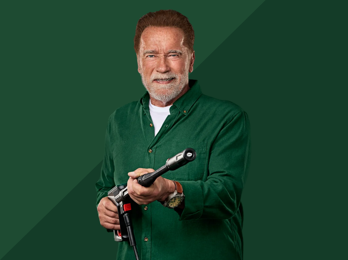 Arnold Schwarzenegger sorridente com uma máquina de lavar de alta pressão.
