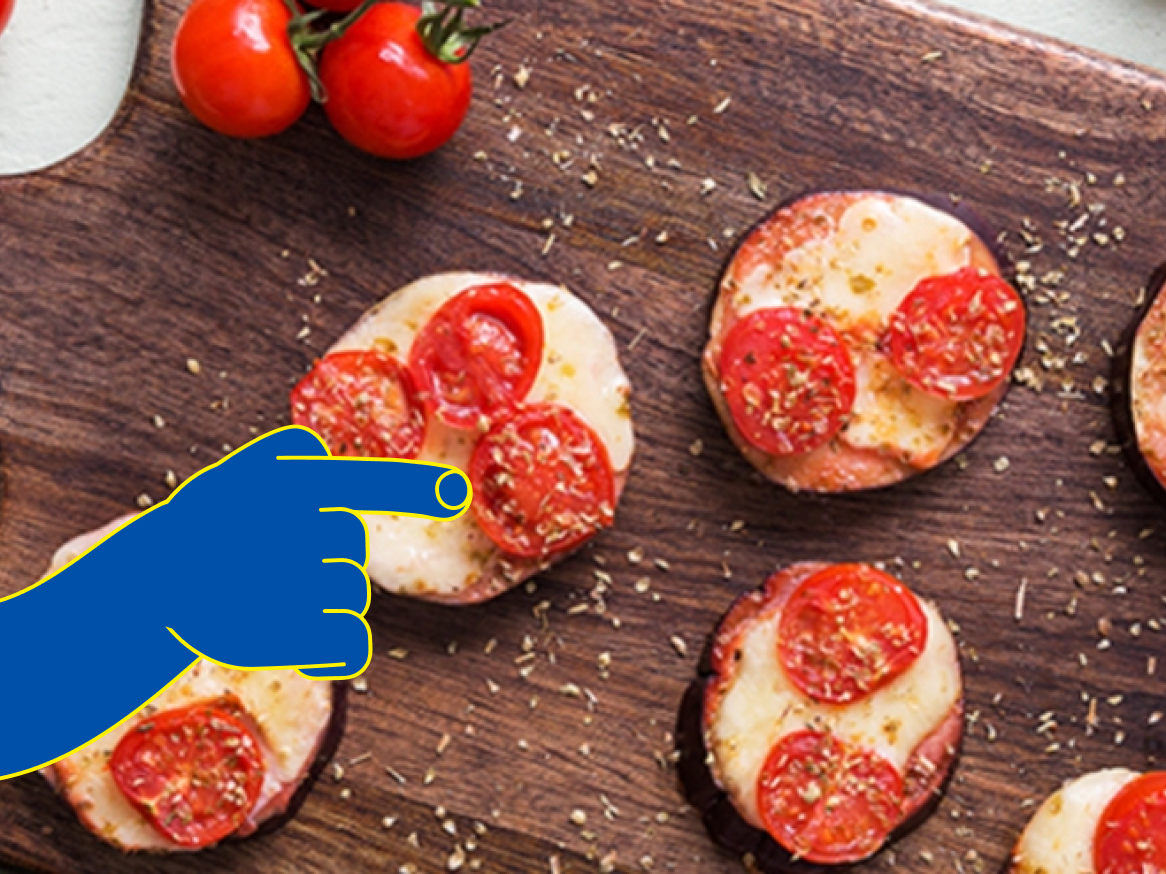 Mini pizzas de beringela com tomate cereja e queijo num tabuleiro de madeira.