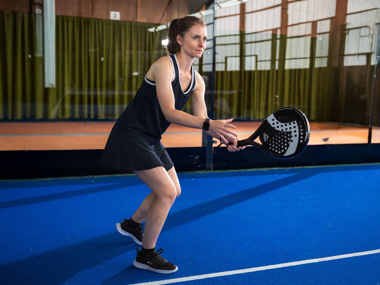 Mulher em vestido de padel preto com raquete de padel preta em campo azul.