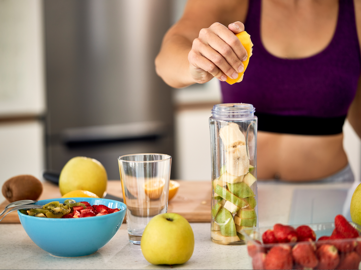 Mulher espremendo laranja em um liquidificador com frutas para um smoothie.
