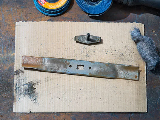 Lâmina de cortador de grama enferrujada em papelão com discos abrasivos e palha de aço.