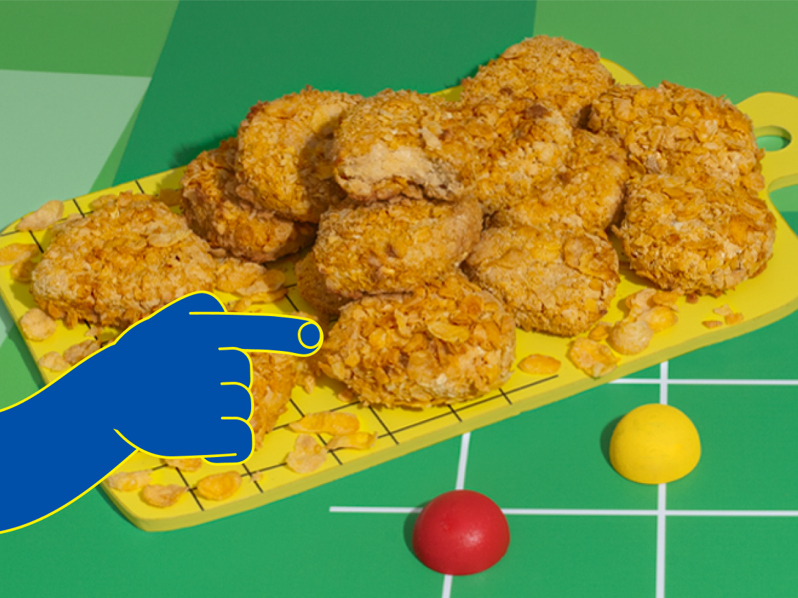 Nuggets de frango empanados com flocos de milho em uma tábua de corte amarela.