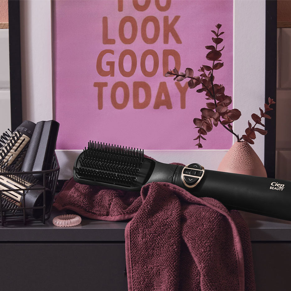 Escova alisadora Cien Beauty sobre uma toalha, com acessórios de cabelo e um pôster.