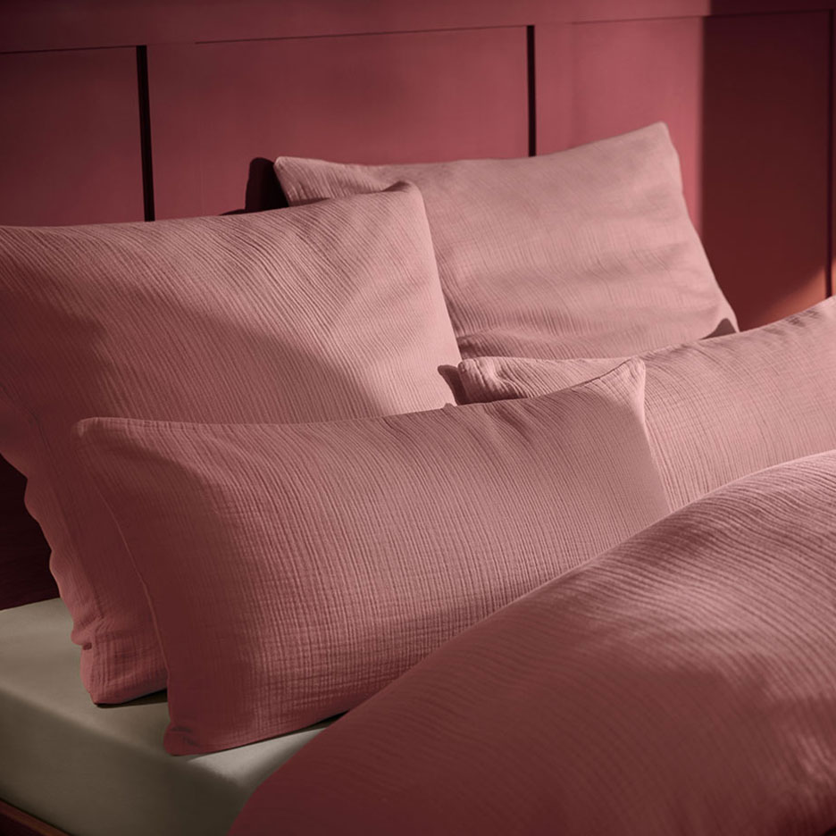 Almofada e roupa de cama de musselina rosa em uma cama com cabeceira de madeira.